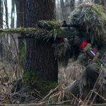 a soldier sniper aiming though the rifle scope in forest