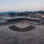 drone view of empty dry grassy baseball field with tribune near various sports grounds against cloud