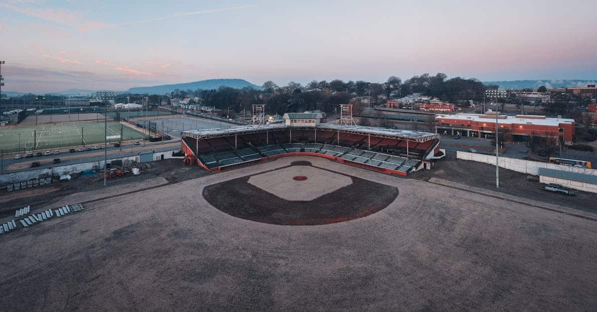 drone view of empty dry grassy baseball field with tribune near various sports grounds against cloud